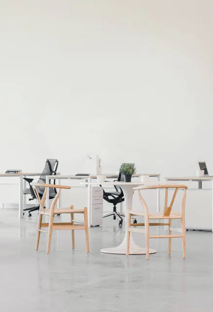 A bright, empty studio with wooden chairs and white desks.