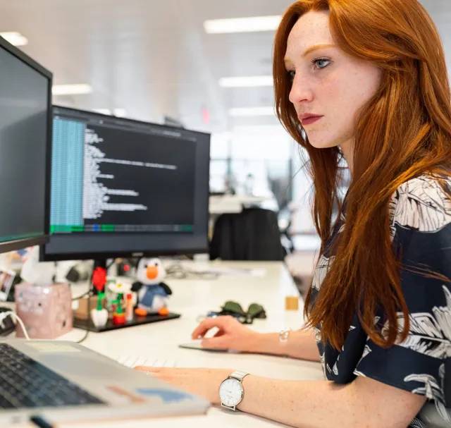 An engineer with red hair reading code on two monitors.